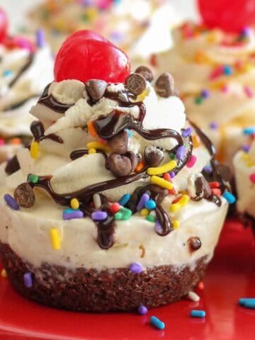 Ice cream cupcake topped with sundae toppings on a red plate.