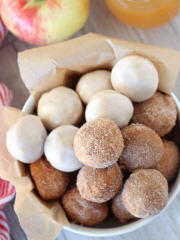 Bowl of apple cider donut holes topped with cinnamon sugar and icing.