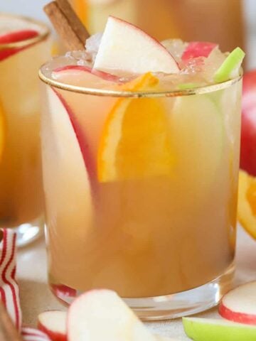 Sangria in a glass garnished with sliced apples, oranges, and cinnamon sticks.