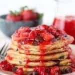 Stack of chocolate chip pancakes covered in strawberry syrup.