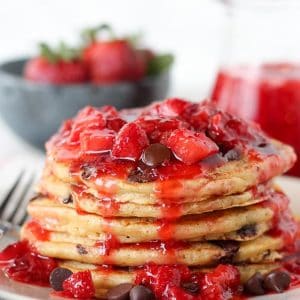 Stack of chocolate chip pancakes covered in strawberry syrup.