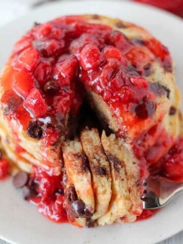 Stack of chocolate chip pancakes covered in strawberry syrup.
