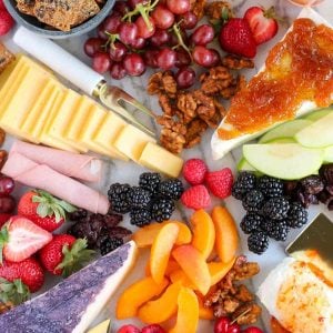 Marble board filled with fruit and cheeses.