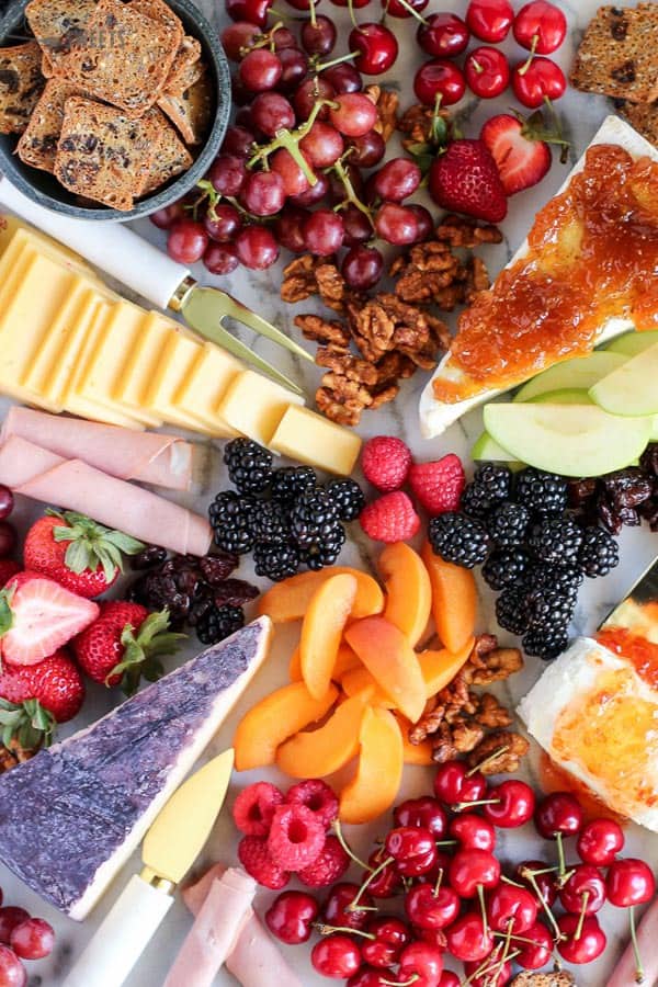 Marble board filled with fruit and cheeses.