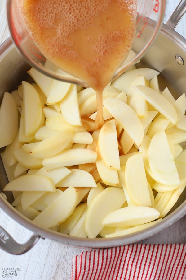 Sliced apples in a pan with syrup and cinnamon being poured over the top.