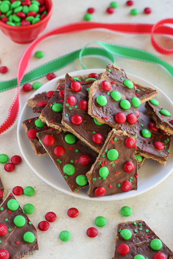 Christmas bark with red and green M&M's on a white plate with red and green ribbon in the background.