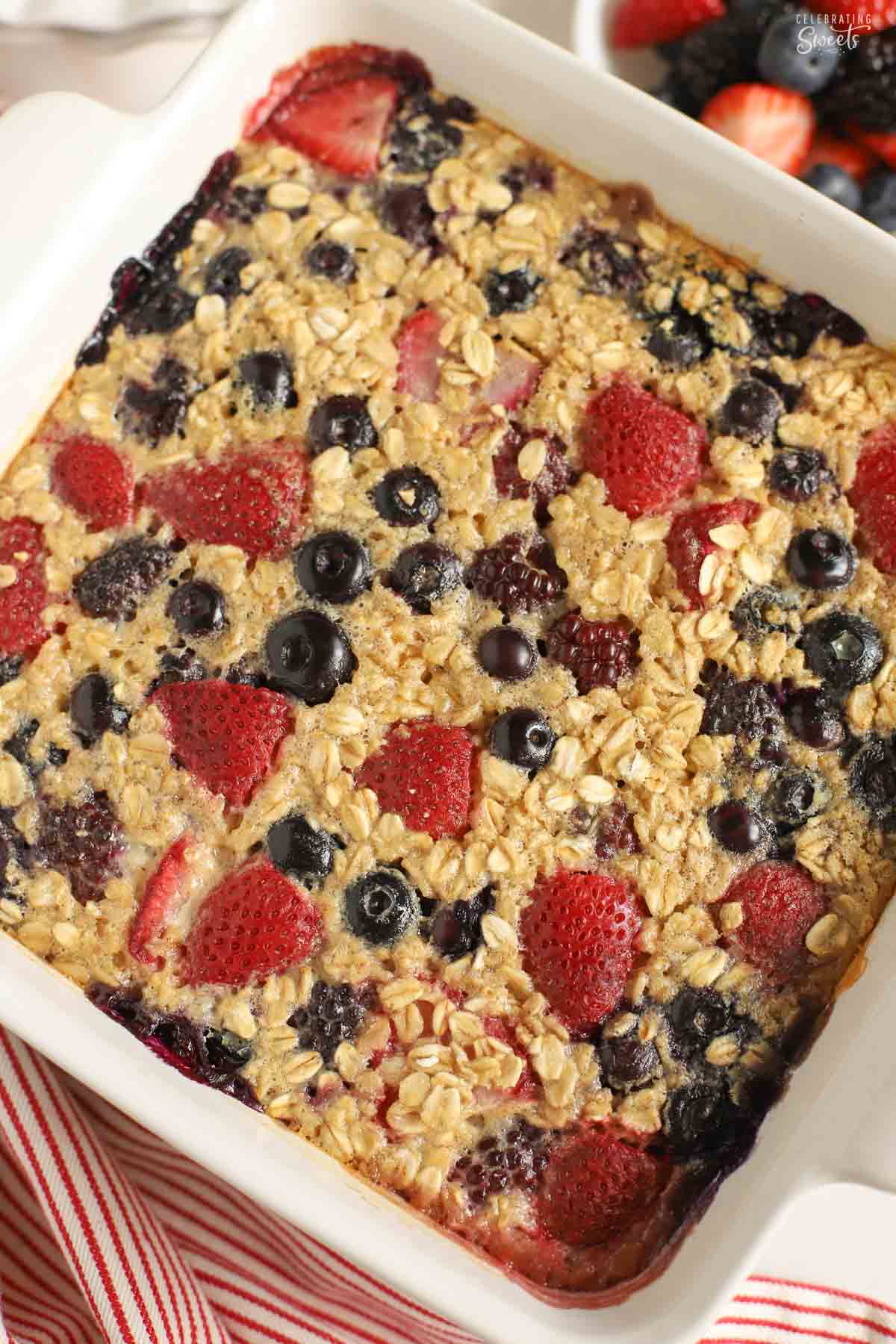 Berry oatmeal bake in a white square baking dish next to a red and white striped towel.
