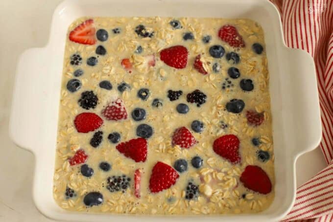 Unbaked oats and berries with liquid in a white square baking dish.