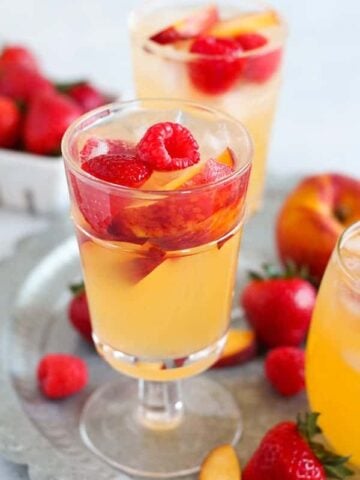Glass of peach sangria with raspberries and strawberries.