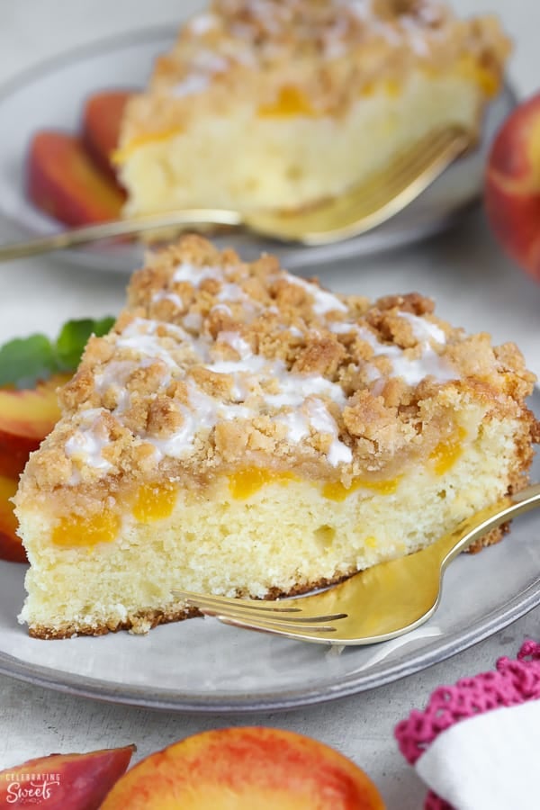 A slice of Peach Crumb Cake on a grey plate with a gold fork.