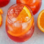 Two aperol spritz cocktails in stemless glasses with a bottle of aperol in the background.
