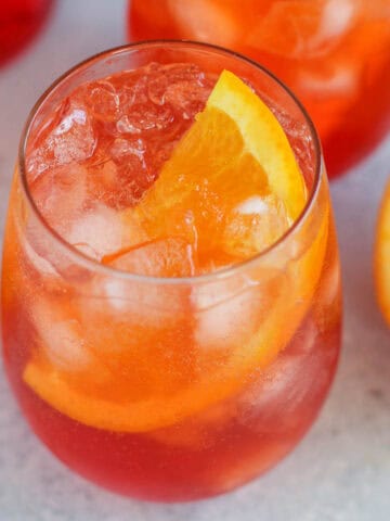 Two aperol spritz cocktails in stemless glasses with a bottle of aperol in the background.
