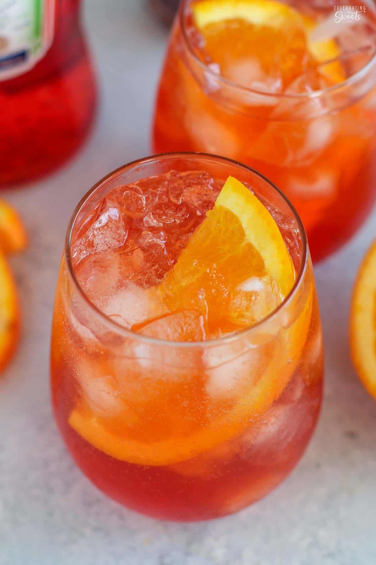 Two aperol spritz cocktails in stemless glasses with a bottle of aperol in the background.