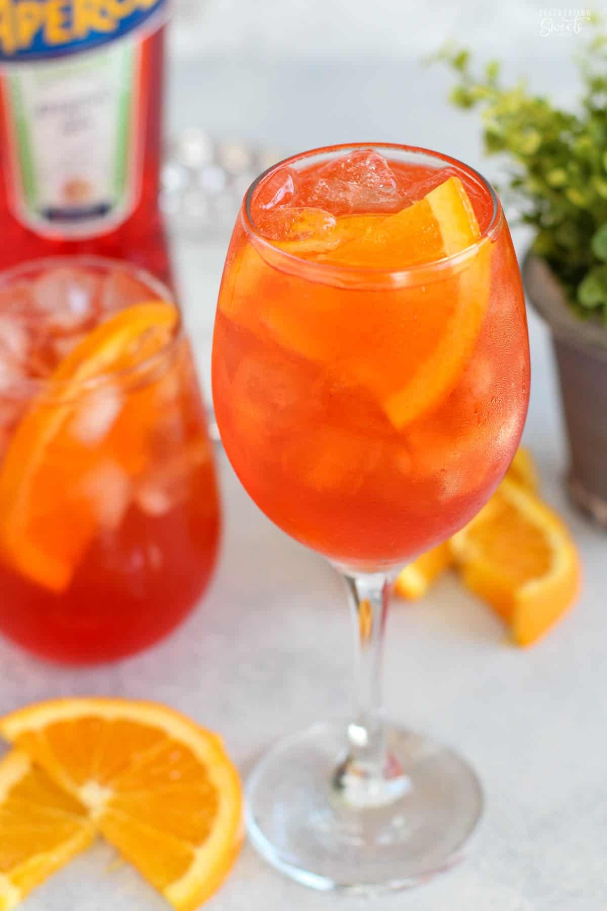 An aperol spritz in a wine glass with a bottle of aperol in the background.