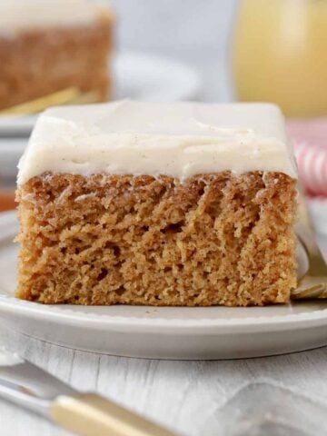 Slice of applesauce cake topped with frosting on a white plate.