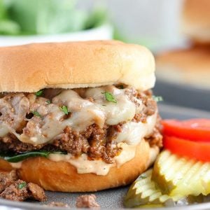 Cheeseburger Sloppy Joe on a grey plate with tomato and pickle.