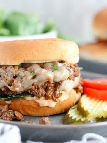 Cheeseburger Sloppy Joe on a grey plate with tomato and pickle.
