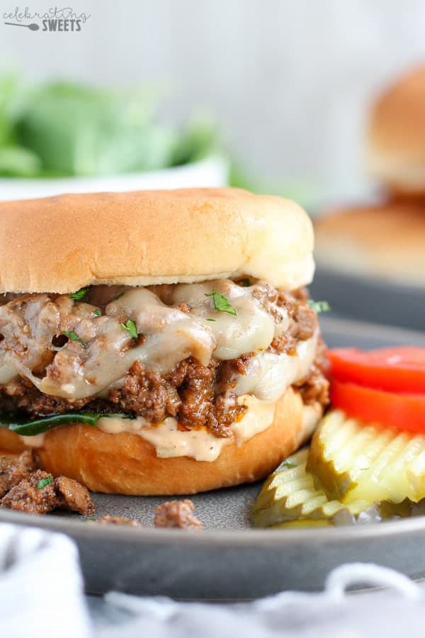 Cheeseburger Sloppy Joe on a grey plate with tomato and pickle.