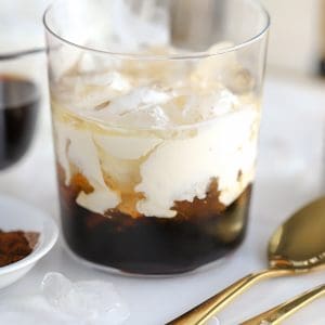White russian cocktail in a glass with two gold spoons on the side.