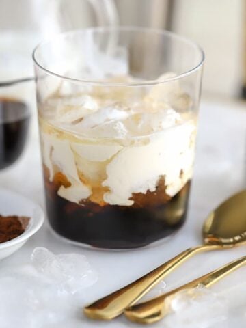 White russian cocktail in a glass with two gold spoons on the side.