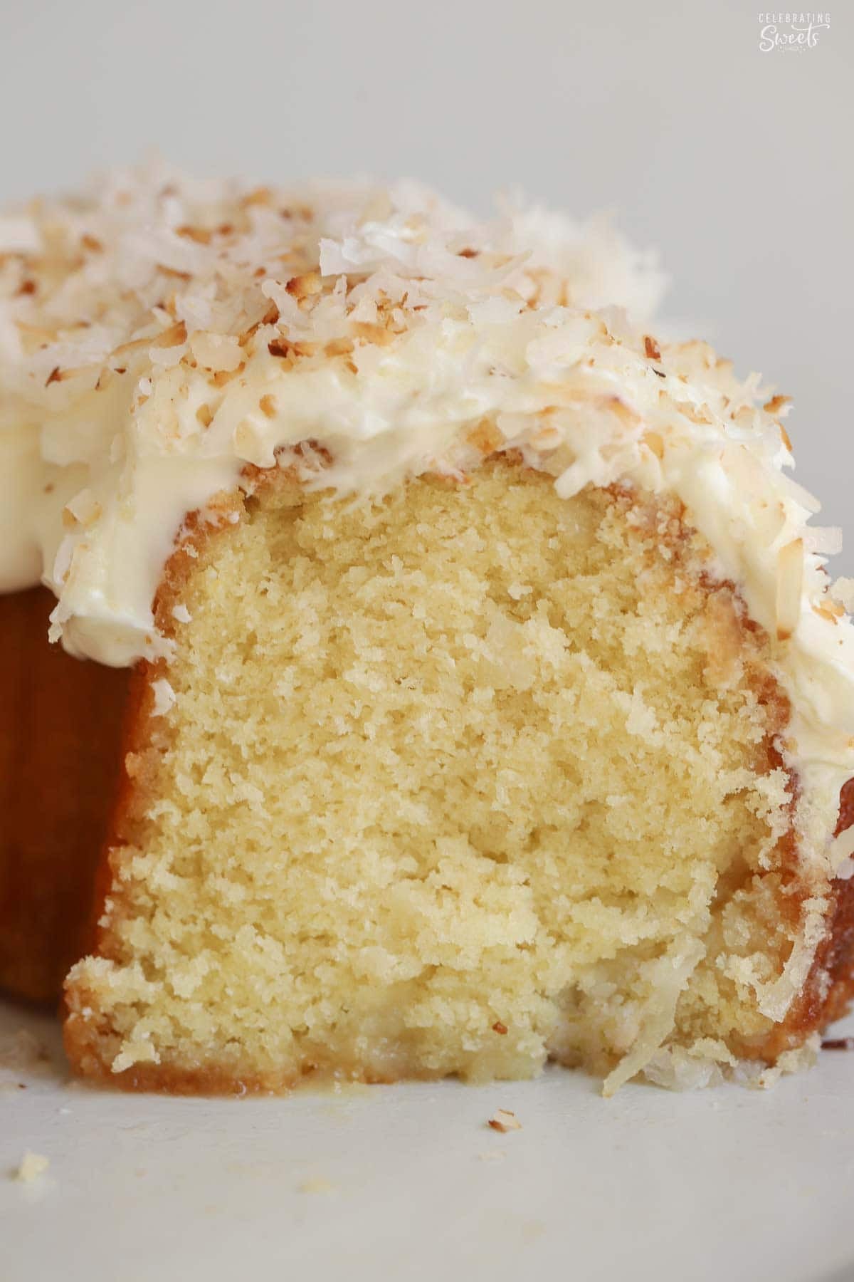Coconut bundt cake topped with white frosting and toasted coconut on a grey plate,