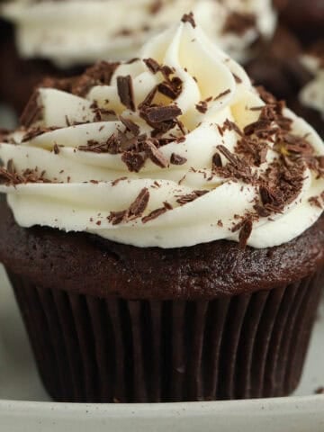 Closeup of a chocolate cupcake topped with cream cheese frosting and chocolate shavings.
