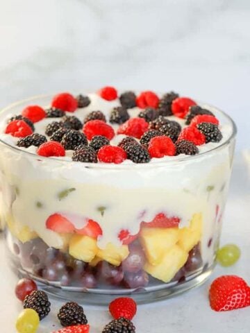 Layered fruit salad in a glass trifle dish topped with pudding and whipped cream.