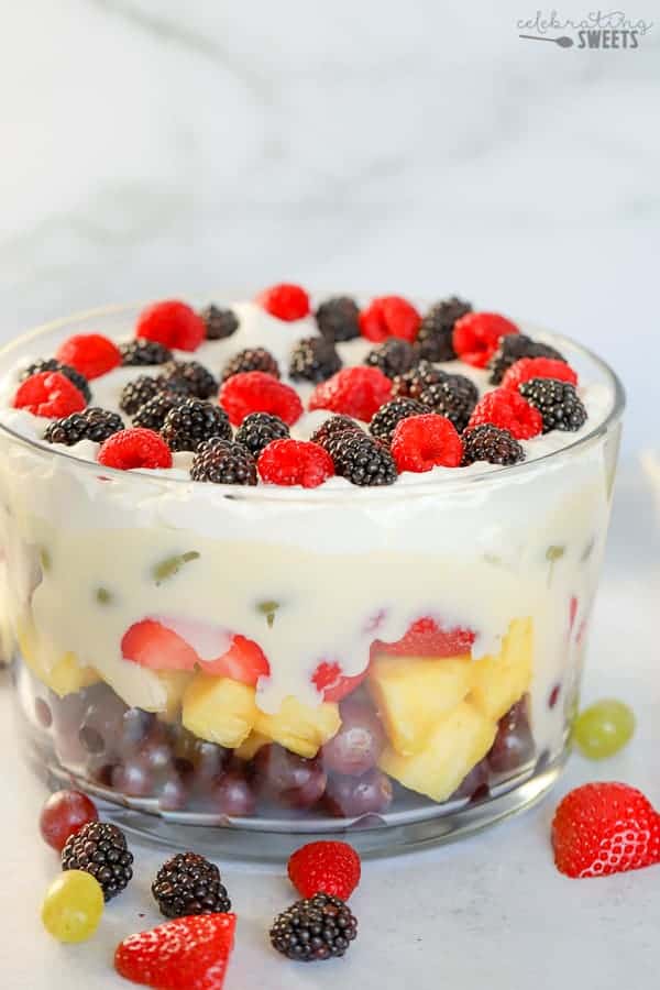 Layered fruit salad in a glass trifle dish topped with pudding and whipped cream.