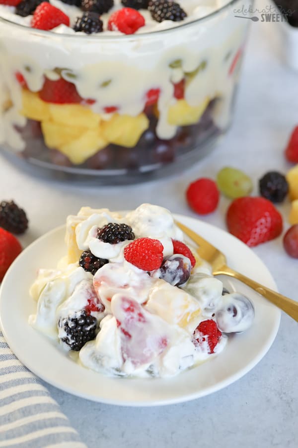 Fruit salad with pudding and white cream on a white plate with a gold fork.