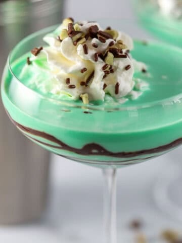 Grasshopper drink in a coupe glass topped with whipped cream and chocolate sprinkles.