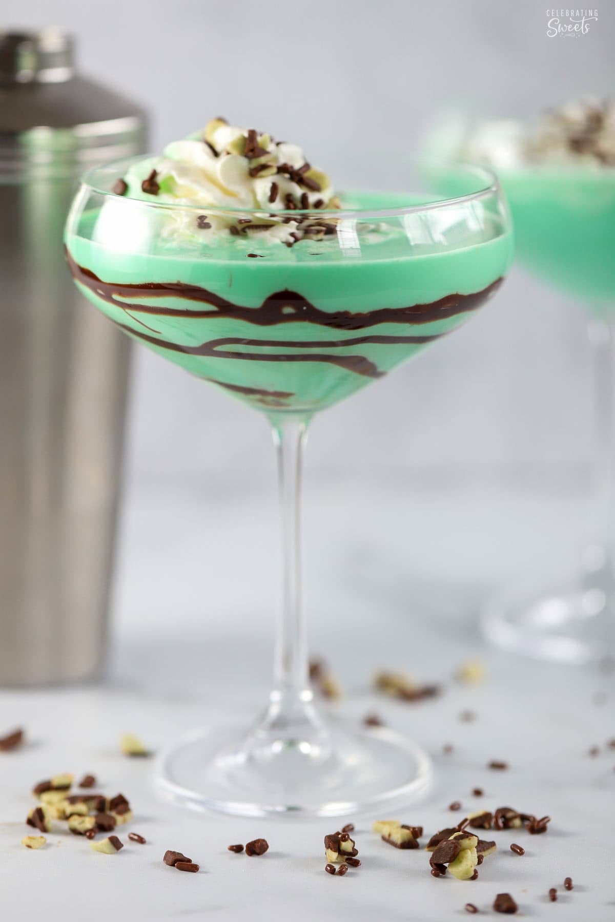 Grasshopper drink in a coupe glass topped with whipped cream. A metal cocktail shaker in the background.