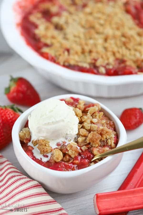 White bowl filled with strawberry rhubarb crisp topped with vanilla ice cream.