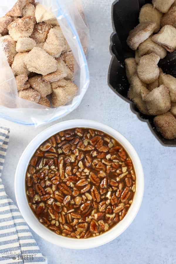 Bowl of caramel pecan sauce with biscuit dough in the background.