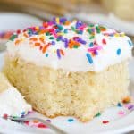 Slice of vanilla cake with vanilla frosting and sprinkles on a white plate.
