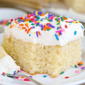 Slice of vanilla cake with vanilla frosting and sprinkles on a white plate.
