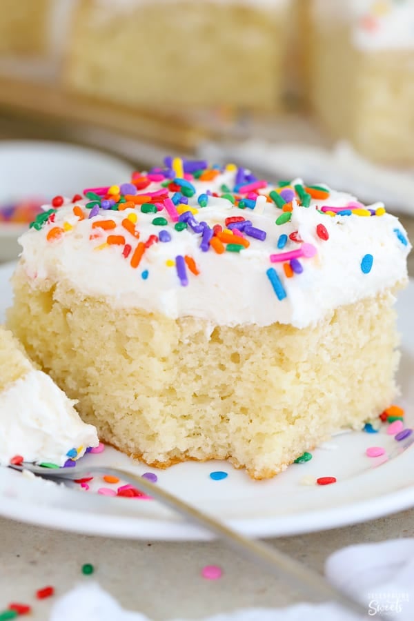 Slice of vanilla cake with vanilla frosting and sprinkles on a white plate.
