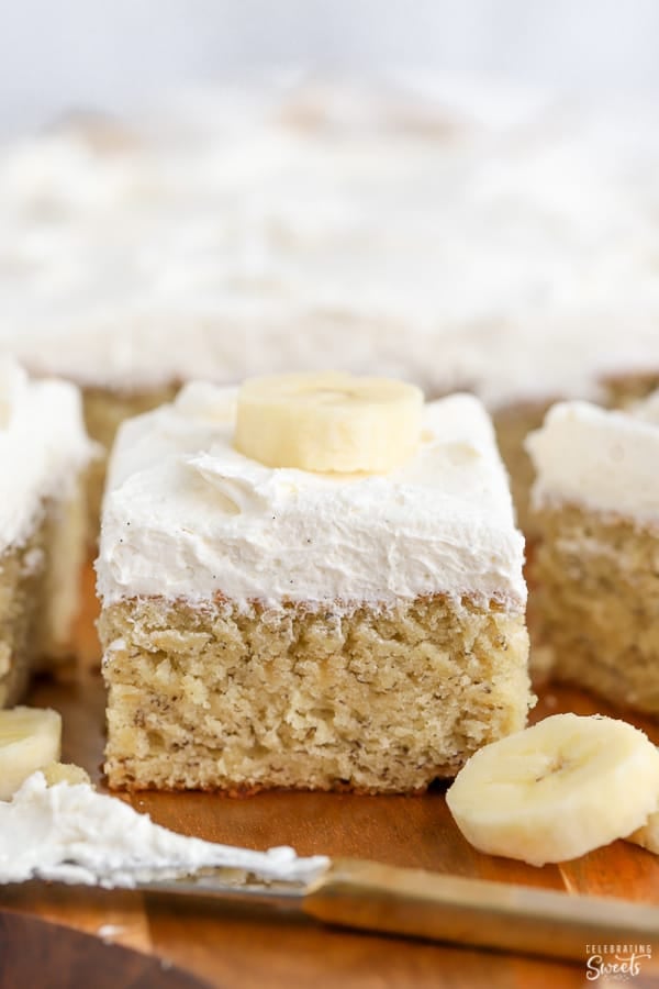 Slice of banana cake topped with vanilla frosting and sliced banana.