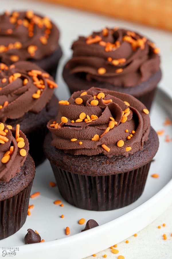 Chocolate cupcakes with chocolate frosting and orange sprinkles on a white plate.