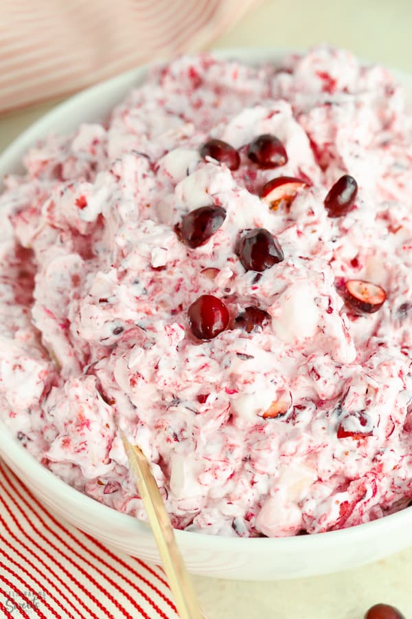 Creamy cranberry salad in a white bowl with a gold spoon.