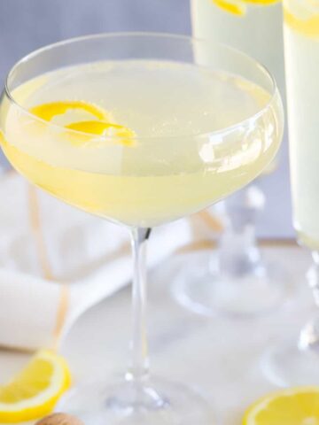 Light yellow French 75 cocktail in a champagne glass topped with a lemon twist.