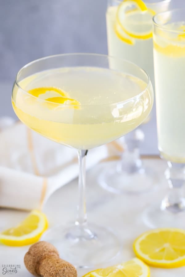 Light yellow French 75 cocktail in a champagne glass topped with a lemon twist.