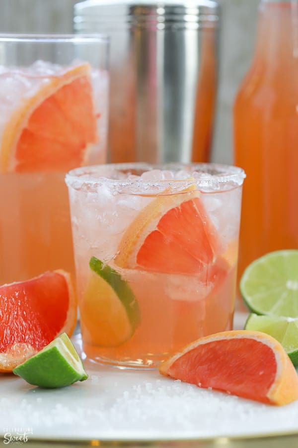 Pink grapefruit cocktail ina glass garnished with lime and grapefruit.