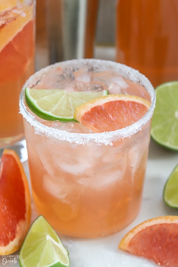 Pink grapefruit cocktail ina glass garnished with lime and grapefruit.