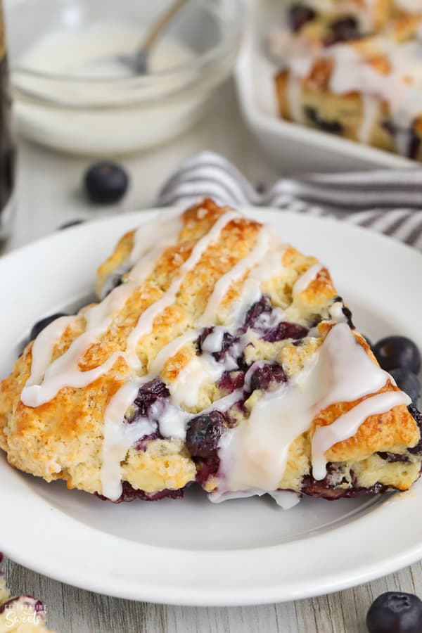 Blueberry scone drizzled with white icing on a white plate.