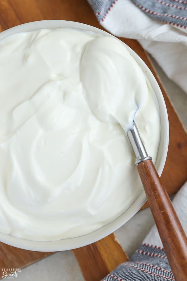 Sour cream in a white bowl with a wooden spoon.