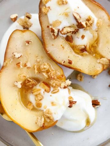 Baked pears on a plate with yogurt and granola.