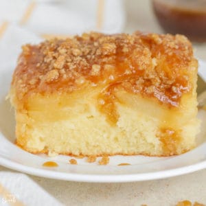 Slice of pineapple cake topped with crumble and brown sugar sauce on a white plate