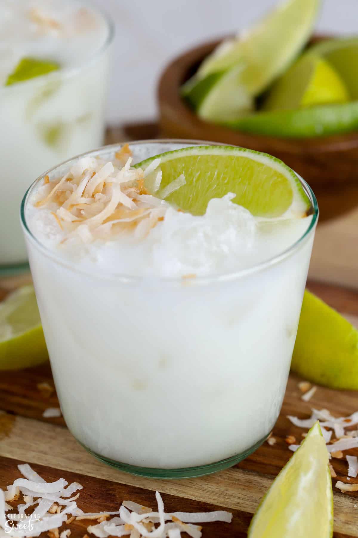Closeup of a coconut margarita in a glass garnished with toasted coconut and lime