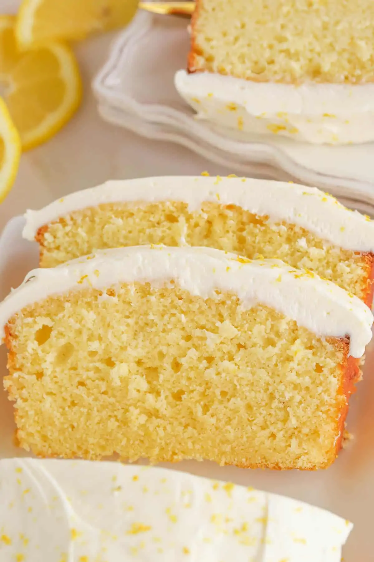 Two slices of lemon loaf cake topped with frosting and lemon zest.