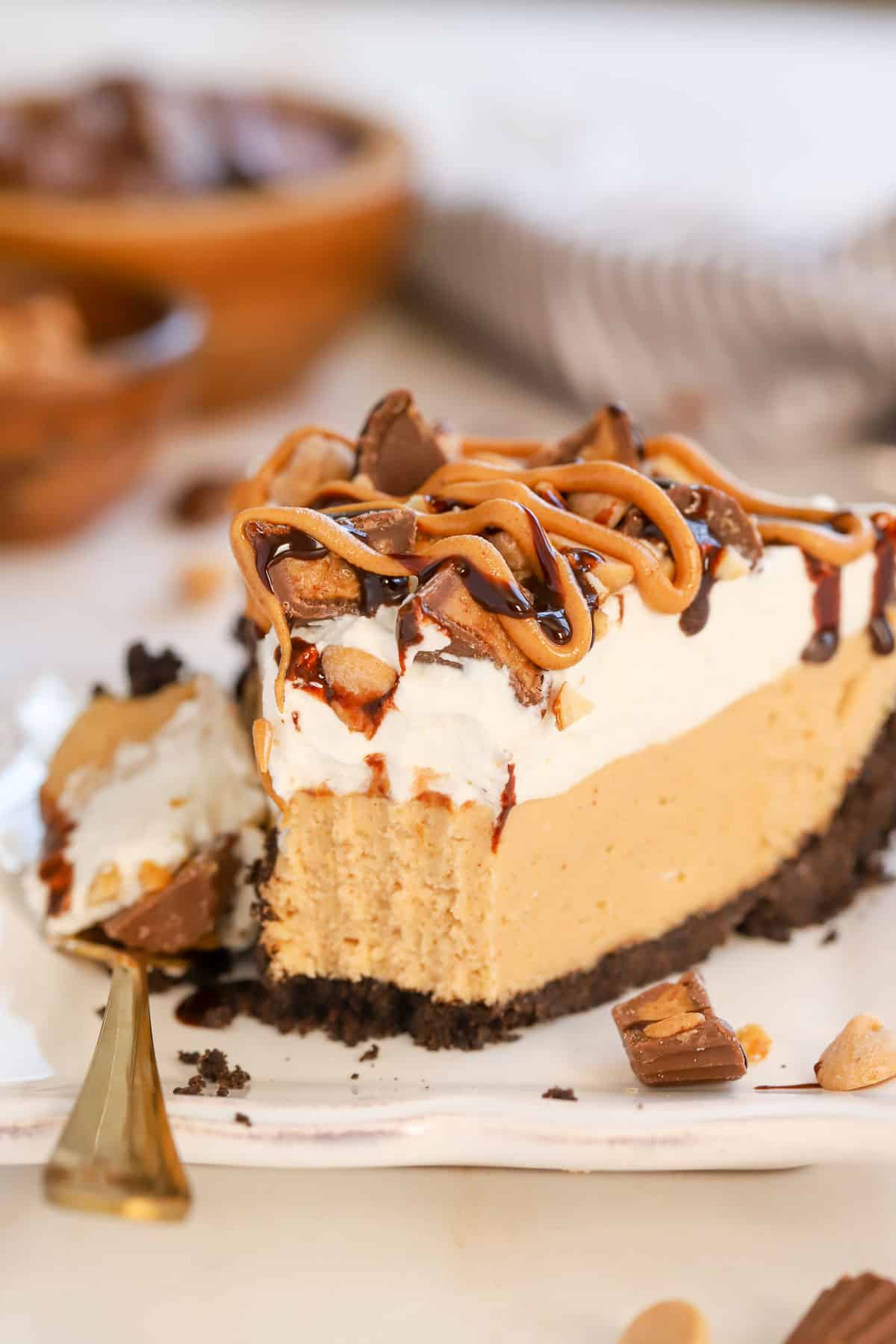 Slice of peanut butter pie topped with chopped peanut butter cups and drizzled with fudge sauce and peanut butter.